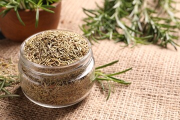 Jar with dry rosemary on burlap fabric, closeup. Space for text