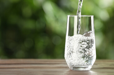 Pouring water into glass on wooden table outdoors, space for text