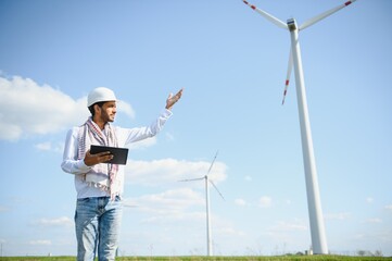 Engineer India man working at windmill farm Generating electricity clean energy. Wind turbine farm generator by alternative green energy. Asian engineer checking control electric power