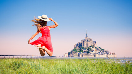 Happy woman with red dress and hat jumping in front of Mont Saint Michel- Normandie in France