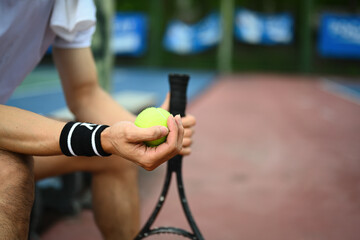 Select focus on hands of male tennis player holding ball racket sitting on the bench at tennis court