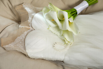 Fototapeta na wymiar Beautiful calla lily flowers tied with ribbon, wedding dress and necklace on sofa