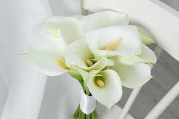 Beautiful calla lily flowers on white chair indoors, closeup