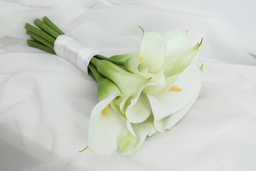 Beautiful calla lily flowers tied with ribbon on white fabric