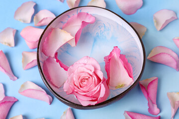 Bowl with water and rose petals on light blue background, above view. Spa composition