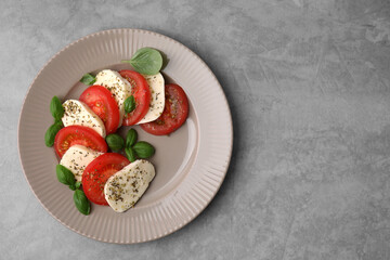 Delicious Caprese salad with tomatoes, mozzarella, basil and spices on light grey table, top view. Space for text