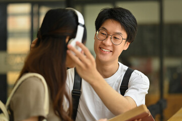 Smiling young asian man wearing headphones to his girlfriend. Lifestyle and love concept