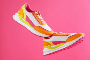 Pair of stylish colorful sneakers in air against pink background