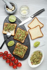 Delicious sandwiches with guacamole and ingredients on white wooden table, flat lay