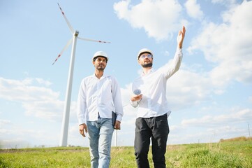indian and european male engineers working on wind farm with windmills.