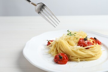 Eating tasty capellini with tomatoes and cheese at white wooden table, closeup. Exquisite presentation of pasta dish
