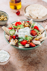 Mediterranean bowl with fried chickpeas, pita, olives, fresh vegetables and tzatziki sauce over beige rustic background