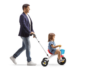 Full length profile shot of a man pushing a girl on a tricycle