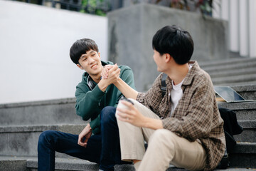 Two smart young Asian college students focusing on his school project, looking at laptop and tablet, discussing and working together at the campus park .