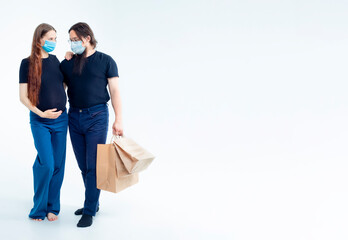young pregnant woman and her husband with shopping bags in medical masks. safety from colds flu and coronavirus on white background. Pregnancy shopping concept happy young family with shopping bags 