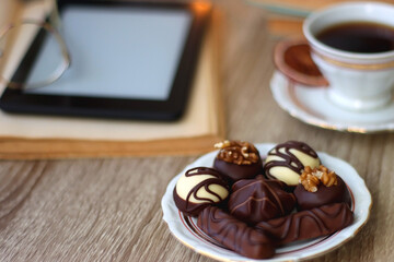 Books, reading glasses, e-reader, plate of chocolate pralines, bowl of cookies, cups of tea and lit...