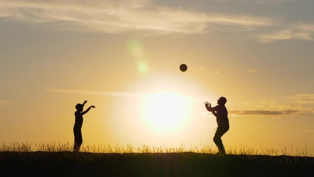 Dad and kid play ball at sunset. Silhouette of a happy family playing volleyball. Active recreation, sports.