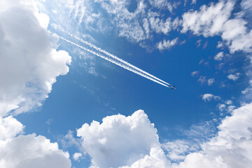 Airliner with contrails flying in a clear blue sky with beautiful cumulus clouds or cumulonimbus. Photography, Full frame. - obrazy, fototapety, plakaty