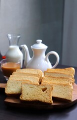 Fototapeta na wymiar Tea Time Snack. Healthy Wheat rusk served with Indian hot masala tea and milk jug over black background. also known as Mumbai cutting chai. with Copy space. Crunchy rusk or toast.