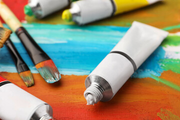 Tubes of colorful oil paints and brushes on canvas with abstract painting, closeup