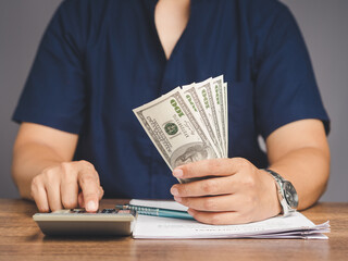 Business people in blue shirts holding US dollar banknotes and using a calculator while sitting in...