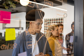 Diverse creative colleagues in discussion brainstorming making notes on glass wall in office