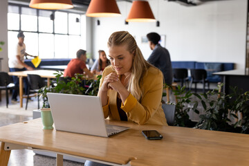 Happy plus size caucasian casual businesswoman making video call using laptop at desk