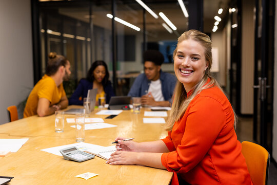 Portrait of happy plus size caucasian casual businesswoman in meeting room mith colleagues