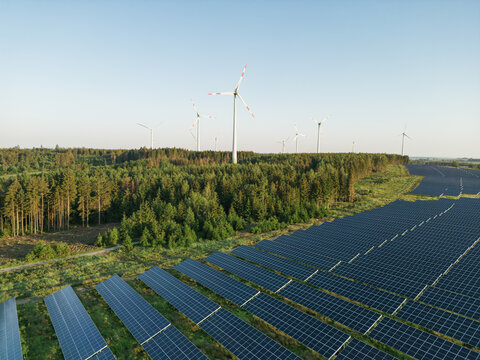 Photovoltaik-Anlage in gr&uuml;ner Landschaft mit Windr&auml;dern im Hintergrund bei Sonnenschein