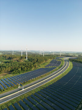 Autobahn zwischen Photovoltaik-Anlagen mit Windr&auml;dern im Hintergrund in gr&uuml;ner Natur bei Sonnenschein