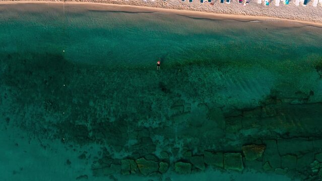 Top-down view of beach with umbrellas in Hanioti (Chaniotis or Chanioti) - small, beautiful tourist village by the sea on Kassandra peninsula, Halkidiki (Chalkidiki), Greece and swimming man.