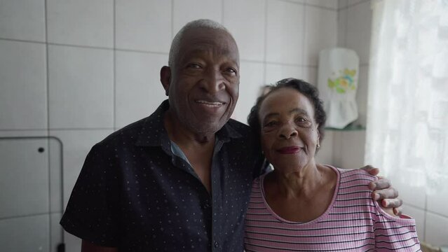 A black senior couple looking at camera with neutral expression standing in home kitchen indoors. A Brazilian African husband and wife