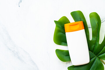 Sun screen products on white background with green leaf. Sun protection. Flat lay image with space for text.