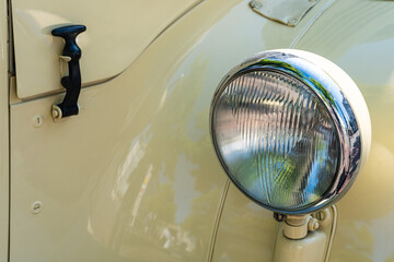 Round lighting headlight on the wing of a yellow vintage car. Closeup.