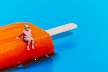 miniature man in swimsuit on a melting orange popsicle
