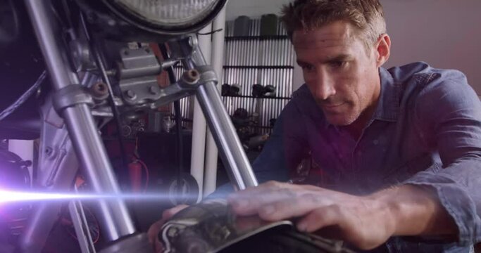 Animation of glowing lights over caucasian male mechanic repairing motorbike in garage