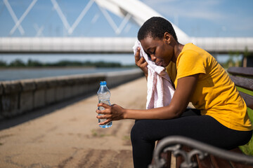 Exhausted woman after exercise drinking water and wiping sweat with towel.