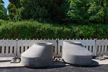 Two concrete parts of sewer manholes at a construction site. Green bushes and trees in the...