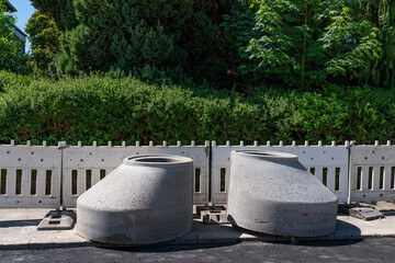 Two concrete parts of sewer manholes at a construction site. Green bushes and trees in the background.