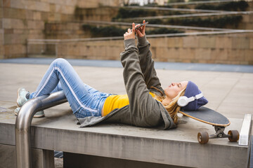 Young woman lying down with head on skate, holding smart phone to have a call or taking selfie, listening music and enjoying contents on line