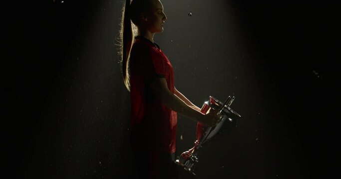 Silhouette of Caucasian woman female soccer football player raising a trophy above head against bright light and falling confetti. Super slow motion, shot on RED cinema camera
