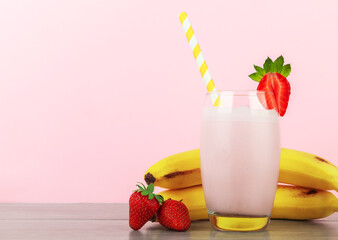 Glass of tasty milkshake with strawberry on table against color background