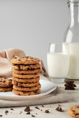 Stack of chocolate chip cookies and glass of milk on white wooden table