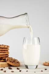 Milk pouring into glass and cookies on wooden table on grey background