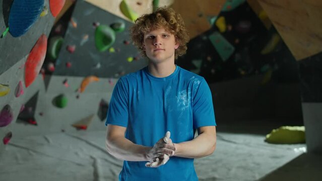 Portrait of a young man climber, guy stands against the background of a climbing wall and use magnesia before climbing.