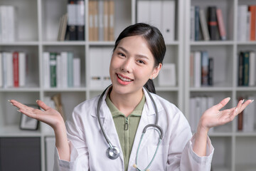 Portrait of smiling young Asian woman doctor show both hands open palms in medical office, smiling and looking at camera