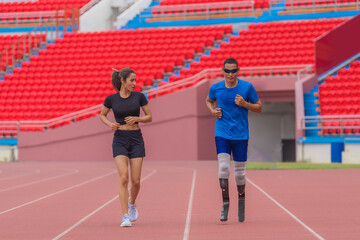 Fototapeta premium A para game speed runner with prosthetic running blades, alongside his female trainer, warms up with a jog on the running track before practice
