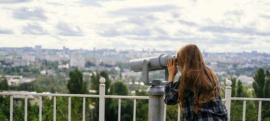 Fototapeta na wymiar Banner shot of a blonde woman looking to the city through some big binoculars.