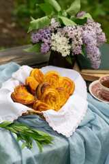 Homemade fresh sugar buns, a bouquet of lilacs and books on a table in the garden - 612797937