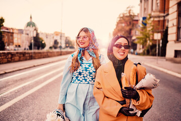 Couple woman one wearing a hijab and a modern yet traditional dress, and the other in a blue dress...